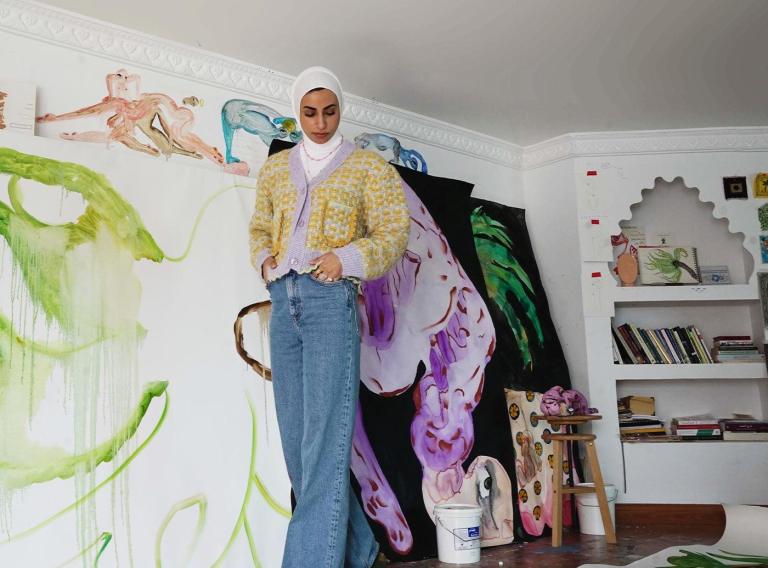 Alymamah Rashed in front of one of her vibrant, nature-inspired artworks, showcasing the themes of identity, nature, and cultural heritage.