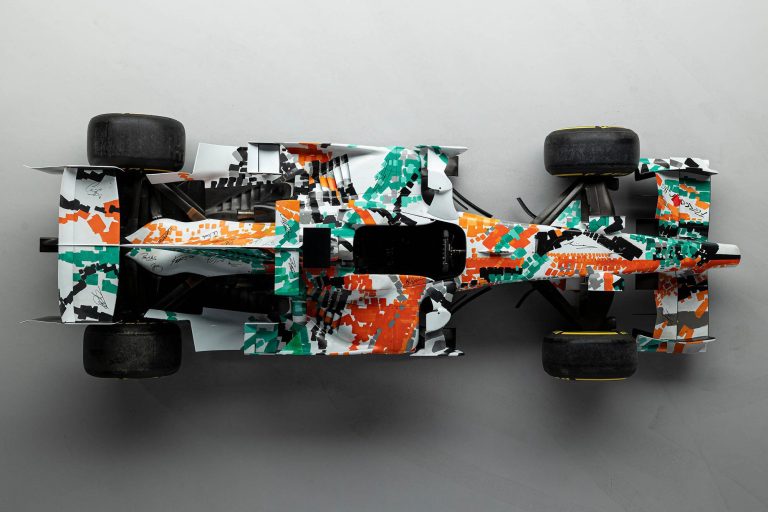 The 2008 Force India VJM01 art car, featuring a green, white, and orange livery designed by Dexter Brown, on display at the Goodwood Festival of Speed.