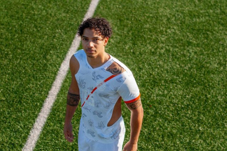 Marshall Islands Football Jersey Raises Climate Change Awareness The Marshall Islands Soccer Federation has launched a powerful football jersey to highlight the threat of rising sea levels. Designed in collaboration with PlayerLayer and Matías Otero, the 2030 No-Home Jersey symbolizes the existential danger the nation faces due to climate change. A Cultural Tribute and Urgent Message The No-Home Jersey incorporates symbols that reflect the nation’s heritage, including the great white shark, the national Plumeria flower, and the outrigger canoe. These cultural elements celebrate the Marshall Islands while conveying a pressing environmental issue. The number “1.5” on the front of the jersey references the Paris Agreement’s critical temperature threshold, emphasizing the risk of irreversible damage if global temperatures rise beyond this point. Though the Marshall Islands has a federation, players, and a football field, it remains the only UN-recognized nation without an official football team. By introducing the jersey, the Federation aims to speed up the process of gaining recognition from the Oceania Football Confederation. It also seeks to raise awareness about the dangers of climate change. Visual Metaphor for Rising Seas Promotional materials for the jersey show it gradually disappearing through cut-outs, symbolizing the potential loss of the Marshall Islands due to rising sea levels. This striking visual is a reminder that, without global action on emissions, the island nation could face permanent flooding within 50 years. Matt Webb, the Federation’s commercial director, explained, “If global warming continues, our nation may be faced with irreversible damage from rising sea waters.” The No-Home Jersey combines a celebration of Marshallese culture with a stark call for climate action. The slogan “we deserve to thrive,” from Marshallese poet Kathy Jetnil-Kijiner, reinforces the message of resilience and the need to protect the nation’s future