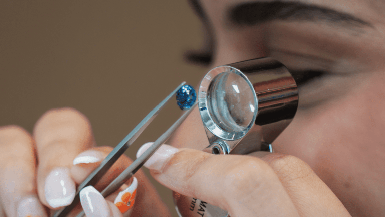 A gemologist closely examining a precious gemstone under a magnifying glass, assessing its cut, clarity, and color during a workshop at L’ÉCOLE Festival.