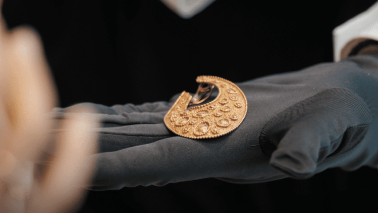 A jeweler using a magnifying glass to engrave delicate patterns onto a gold pendant, demonstrating traditional craftsmanship techniques.